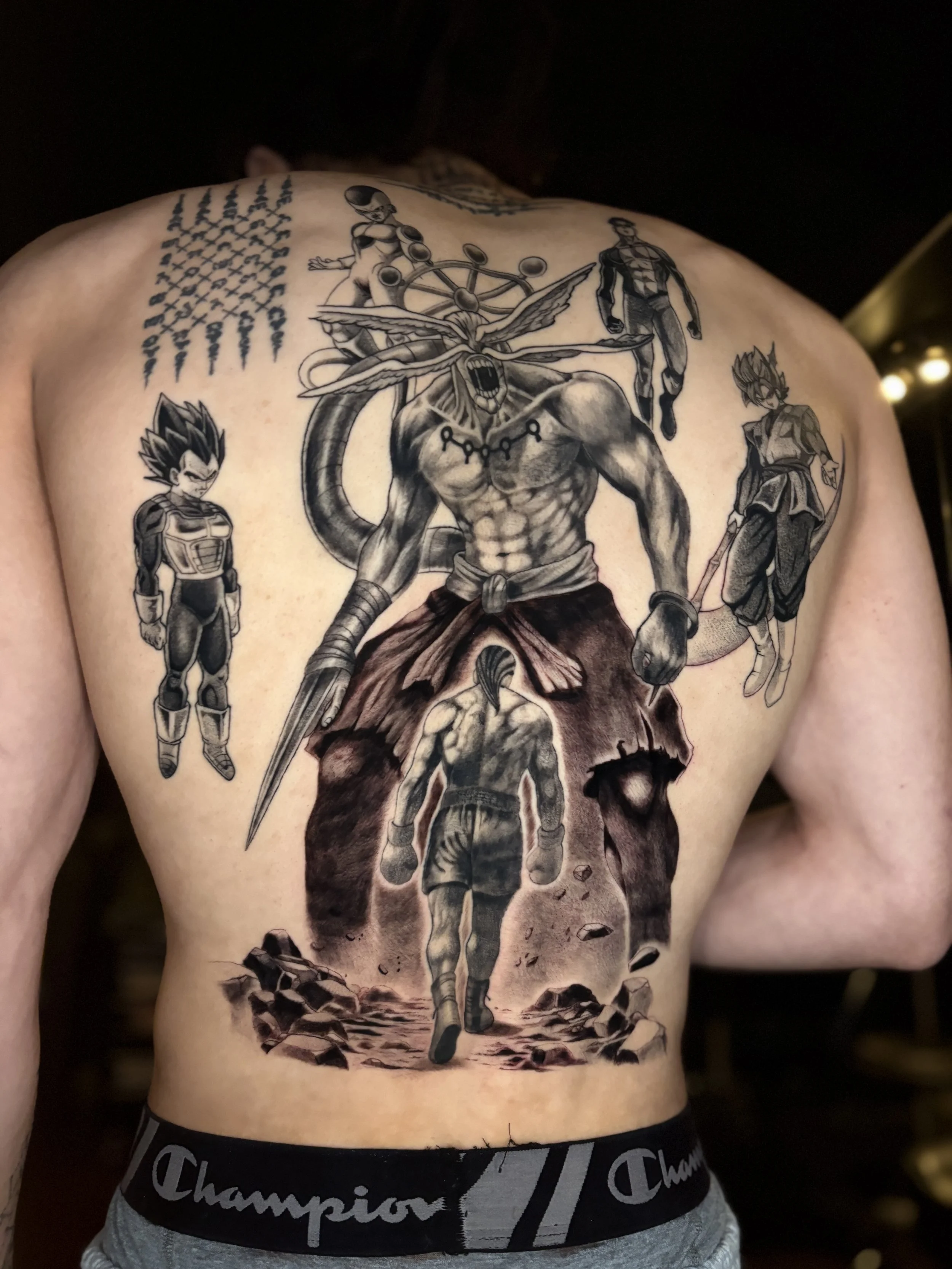 A detailed black and gray tattoo covering the person's back, featuring characters from anime and manga, including a muscular character with a staff, two standing characters in armor, a flying insect, a female character with a split top, and a scene of rocky ground with debris.