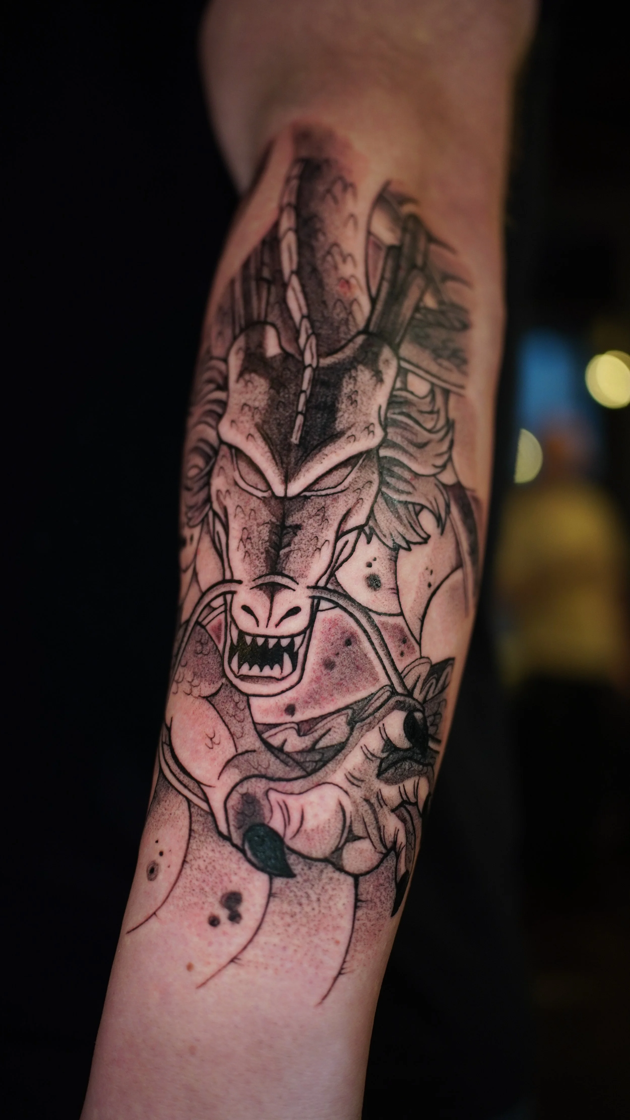 Close-up of a tattoo on a person's arm featuring a fierce lion's face with a mane, snarling with sharp teeth showing, in black ink with detailed line work.