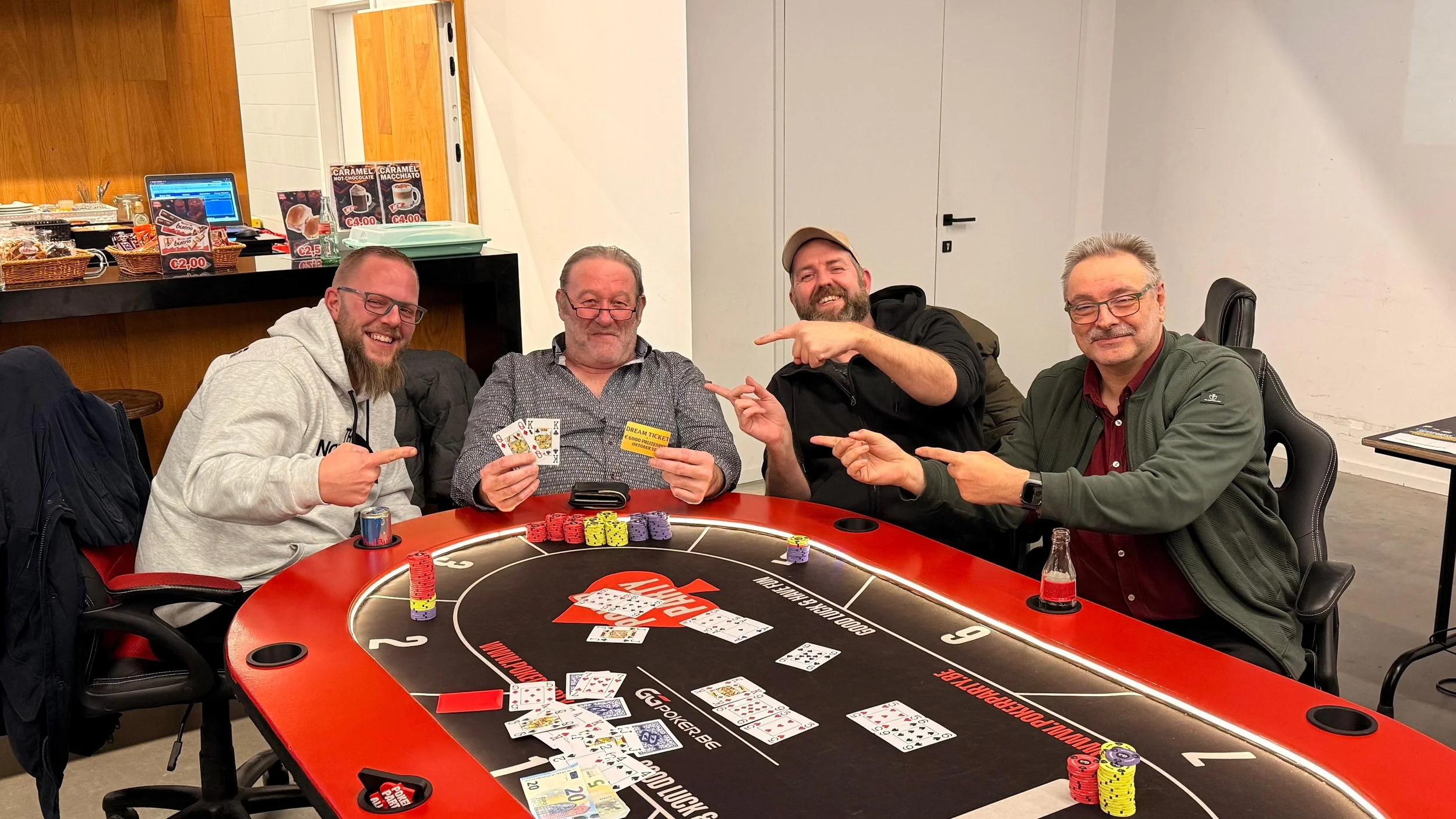 Vier mannen zitten aan een poker tafel, vieren dat ze hebben gewonnen, met pokerkaarten en fiches. Ze lachen en wijzen naar elkaar.