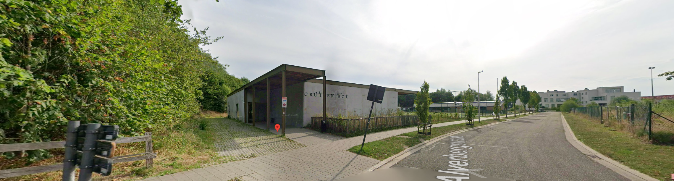 Een modern gebouw met de naam 'Cruttenhof' op de gevel, gelegen aan een straat met fietsen, bomen en lage regelgeving, onder een overkapping, met een groene omgeving op de achtergrond.