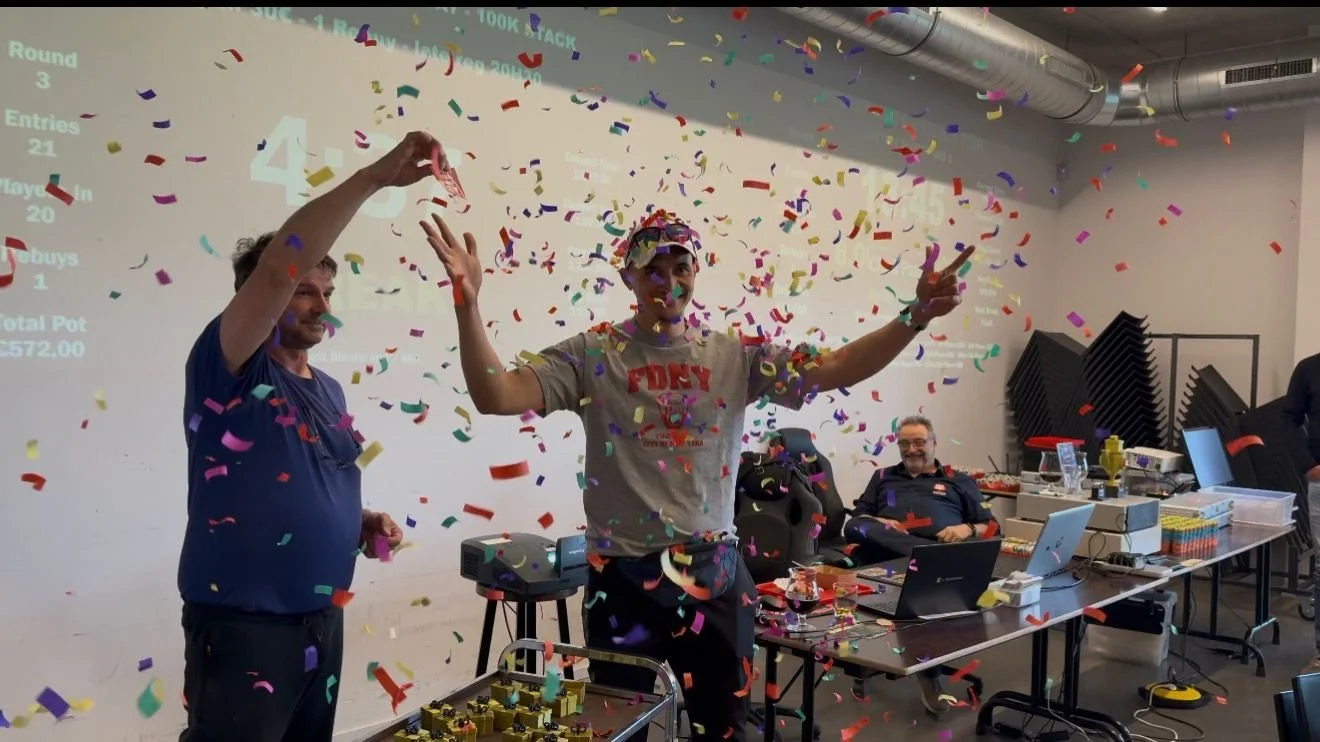 Manen vieren met confetti in een kantoorruimte of vergaderzaal, met drie mensen die achter een tafel zitten en een computer, een smartwatch, en andere kantoorartikelen op de tafel.