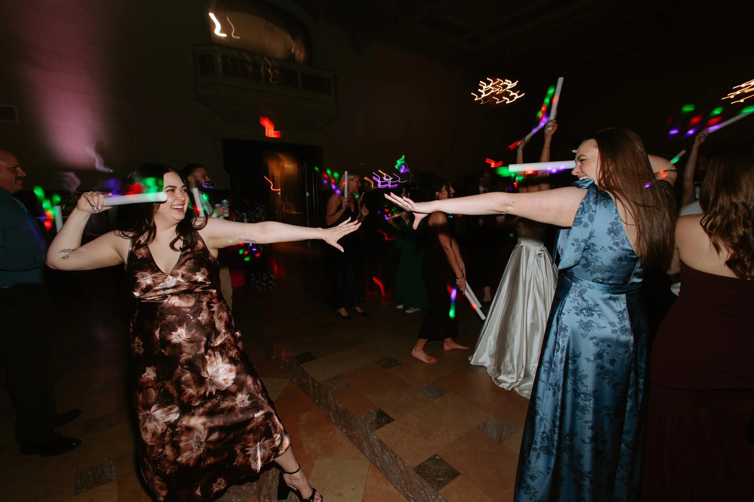 People dancing at a party with colorful light sticks in a dimly lit room.