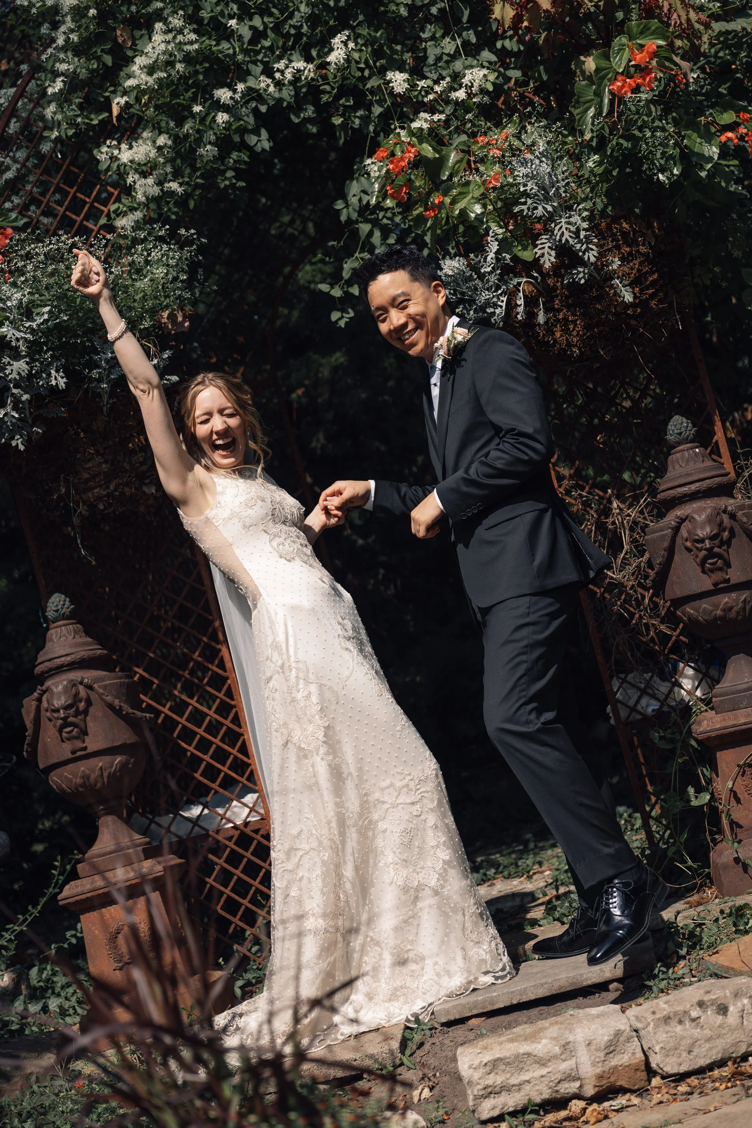 Happy bride and groom dancing outdoors in a garden setting surrounded by greenery and flowers.
