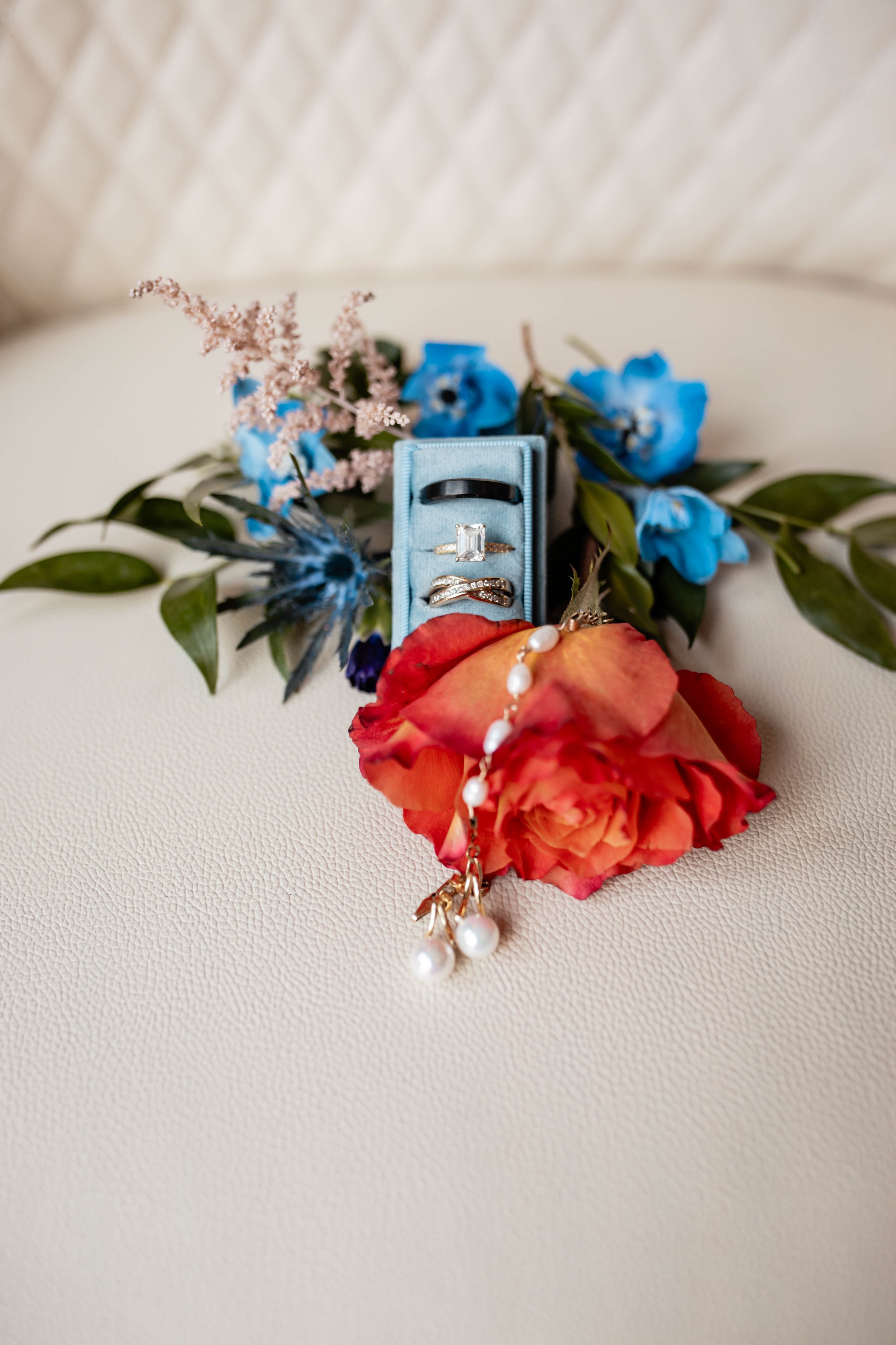Flowers, rings, and jewelry laid on a white surface with a beige textured background.