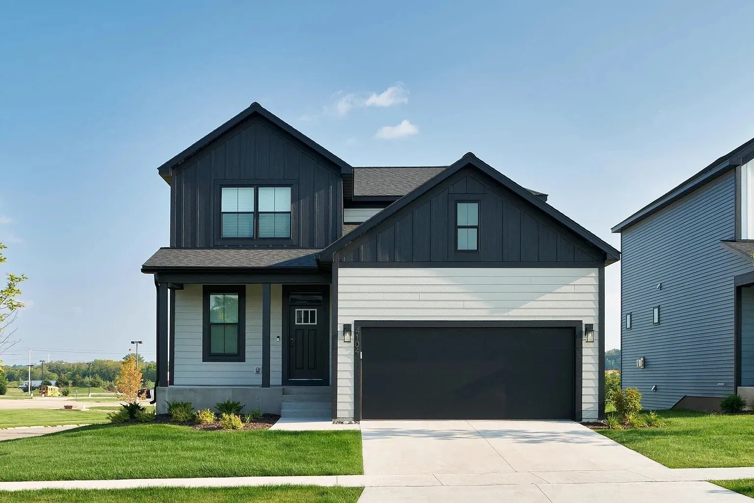 Modern two-story house with gray and black siding, black garage door, front steps, small front lawn, and a driveway, under a clear blue sky.