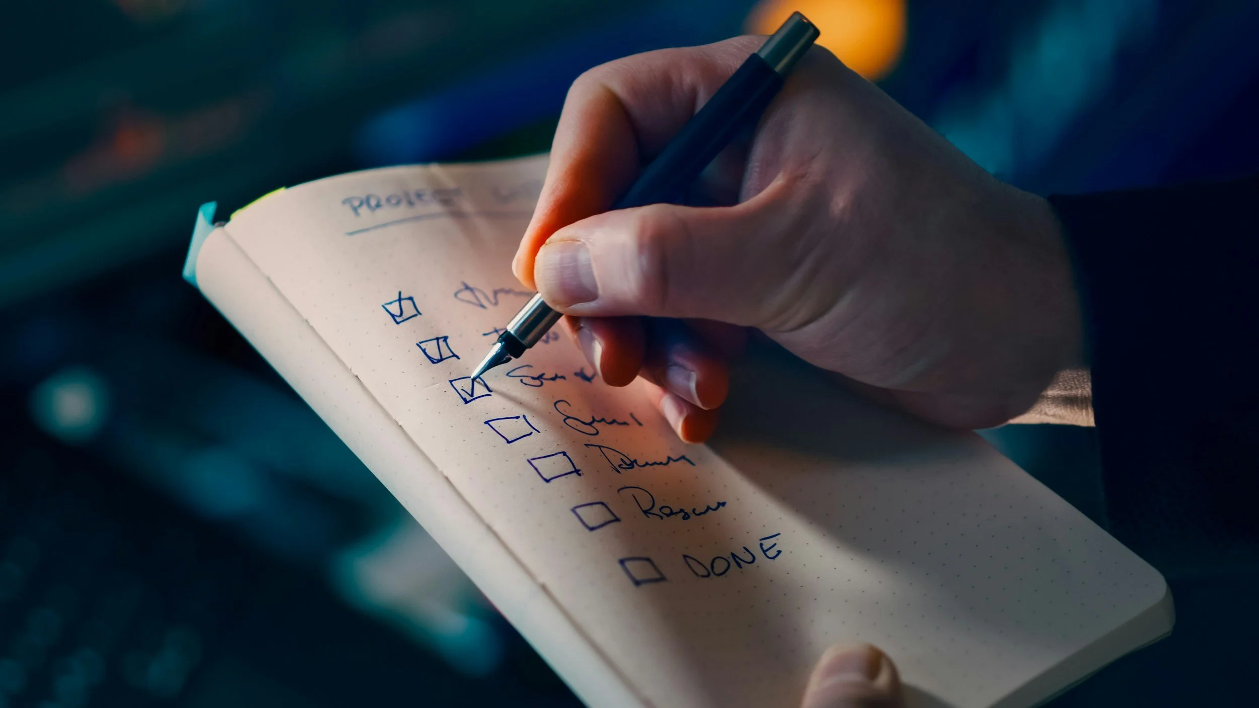 A person writing a to-do list on a notepad with a black pen, with checkboxes next to listed tasks.