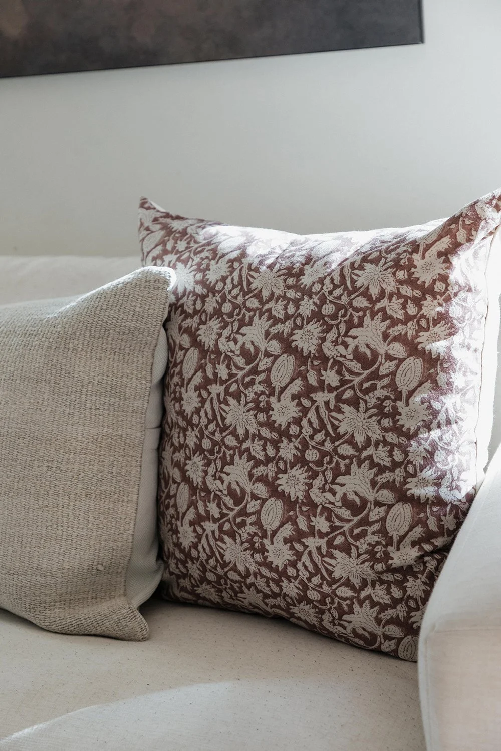 Close-up of a beige fabric cushion and a decorative pillow with a floral pattern on a light-colored sofa