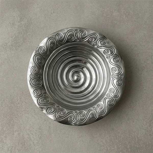 Silver metal decorative plate with a spiral pattern and intricate swirling designs around the edge.