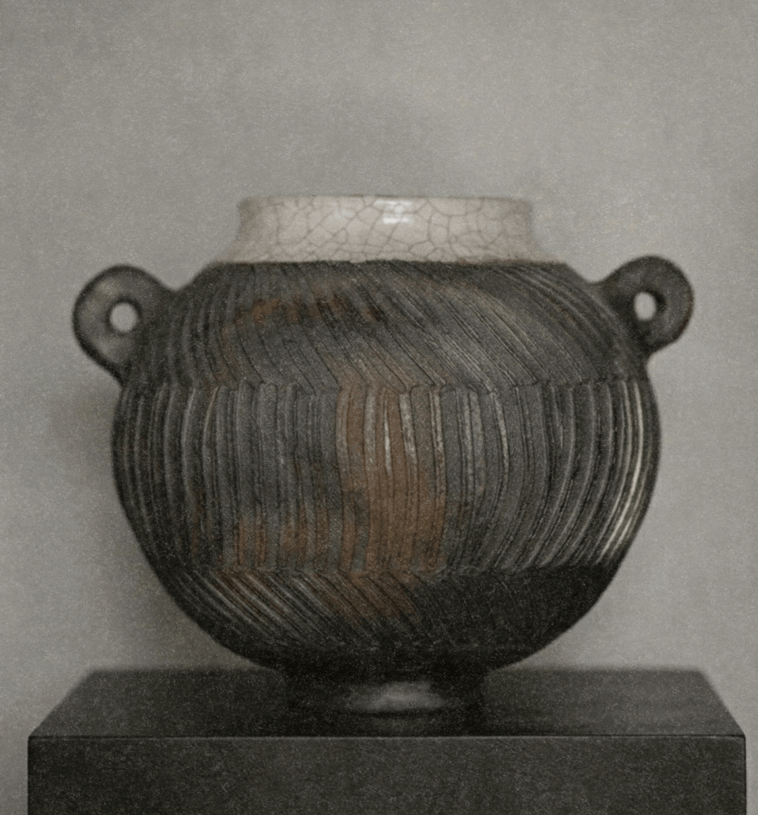 A large ancient ceramic vessel with two small handles, featuring a textured, dark striped pattern, displayed on a pedestal.