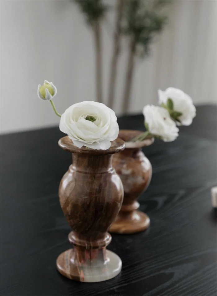Two brown marble vases with white flowers on a black table, blurred background.