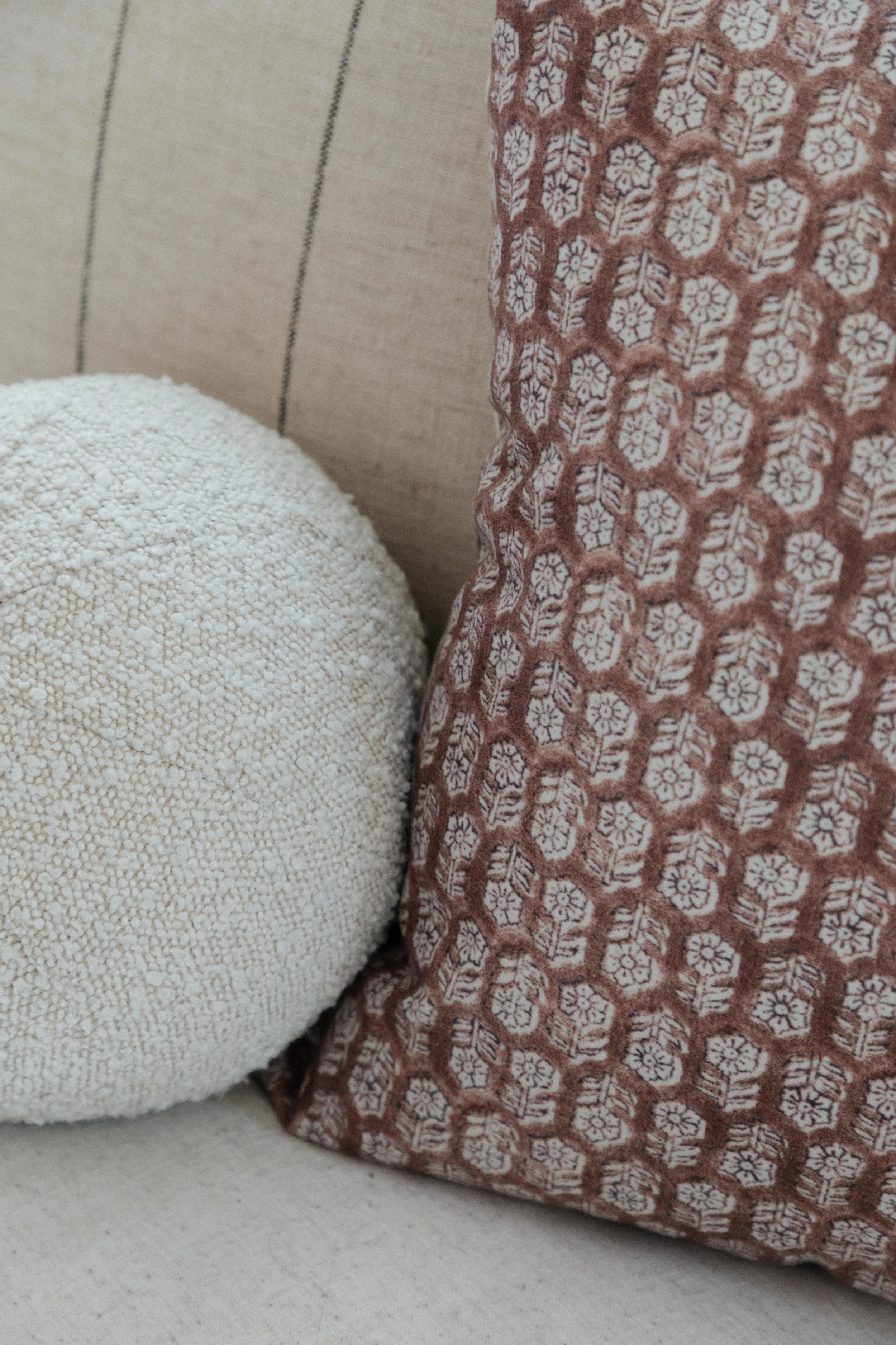 Close-up of a pillow with a white textured cover and a cushion with a red and white floral pattern on a beige fabric background.