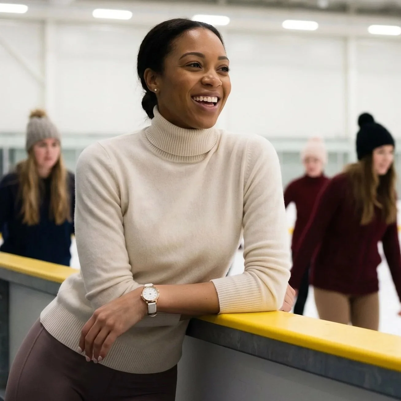 A young woman stands leaning on the barrier at the side of an ice rink wearing a warm turtleneck jumper and an elegant wristwatch as skaters move in the background