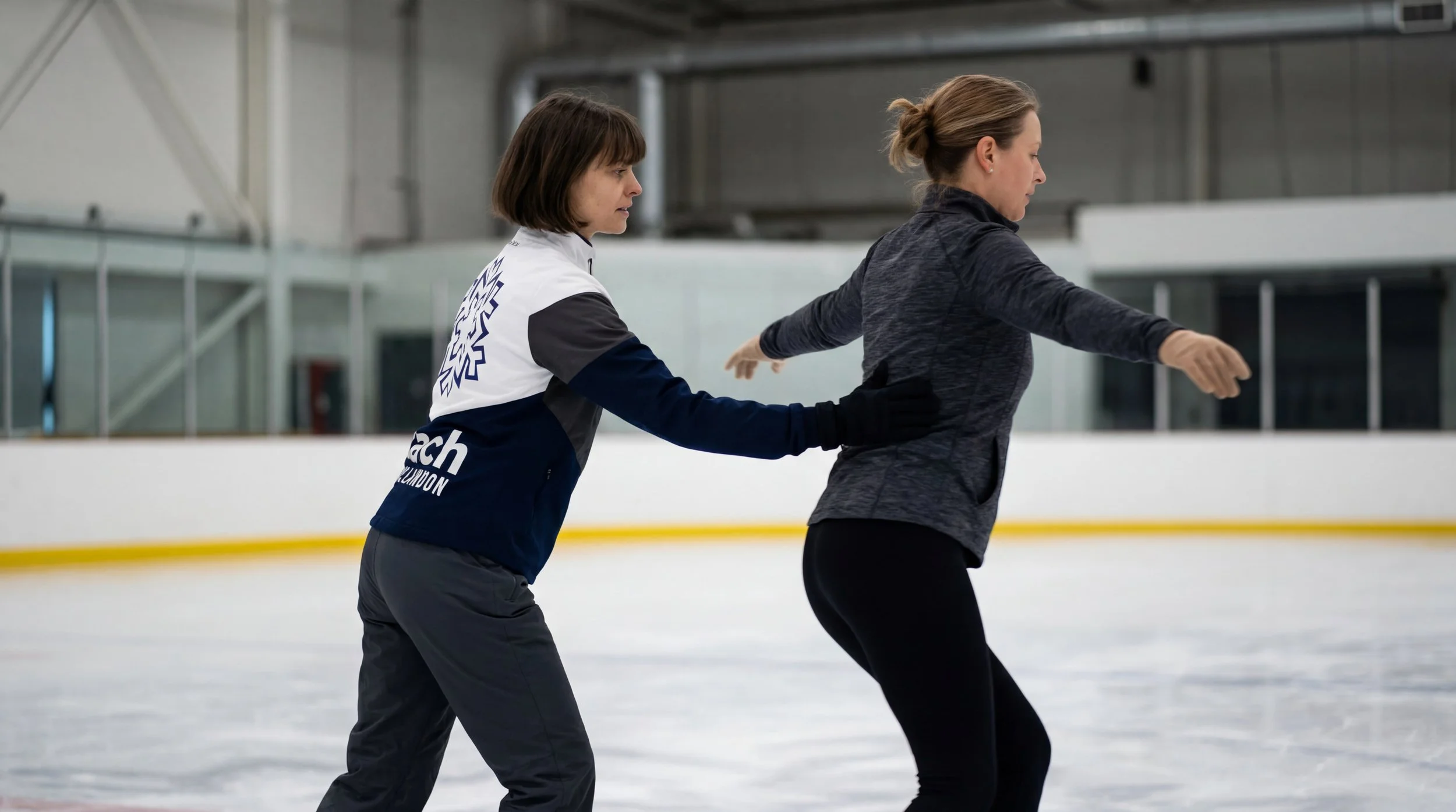 Two women, one a coach and the other a student, figure skating on the ice rink.