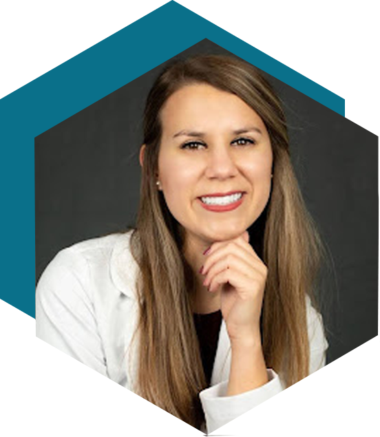 Professional headshot of a smiling woman with long, straight brown hair, wearing a white blazer and resting her chin on her hand. The image is cropped into a hexagonal shape