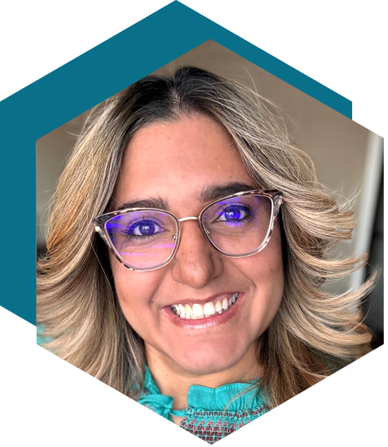 Smiling woman with shoulder-length blonde hair and glasses, wearing a light blue top, in front of a dark background framed in a hexagon shape.