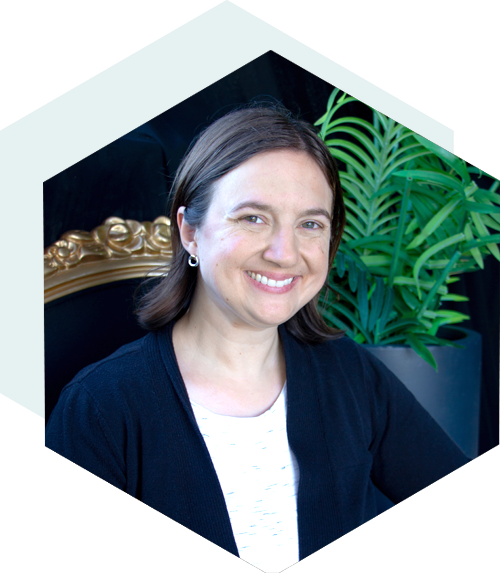 Smiling woman with dark hair sitting in front of a black background with a plant to the right in a hexagon shape