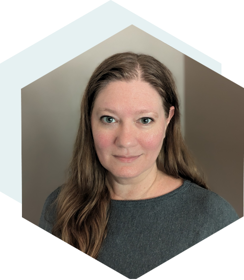 Woman with long light brown hair wearing a dark gray top, smiling softly, framed in a light blue hexagon shape.