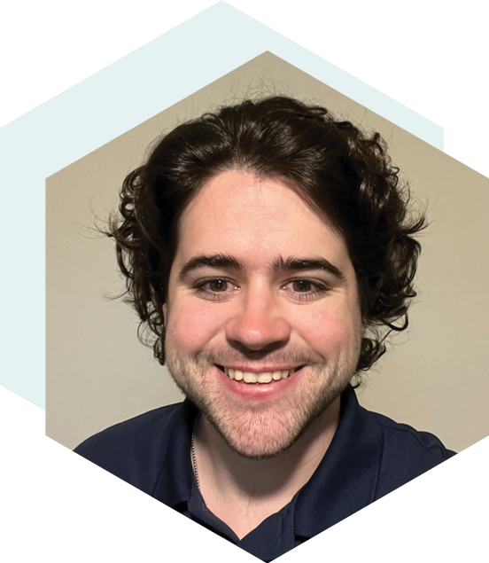 Smiling man with curly dark hair wearing a navy blue shirt, set against a neutral background with a hexagonal design overlay.