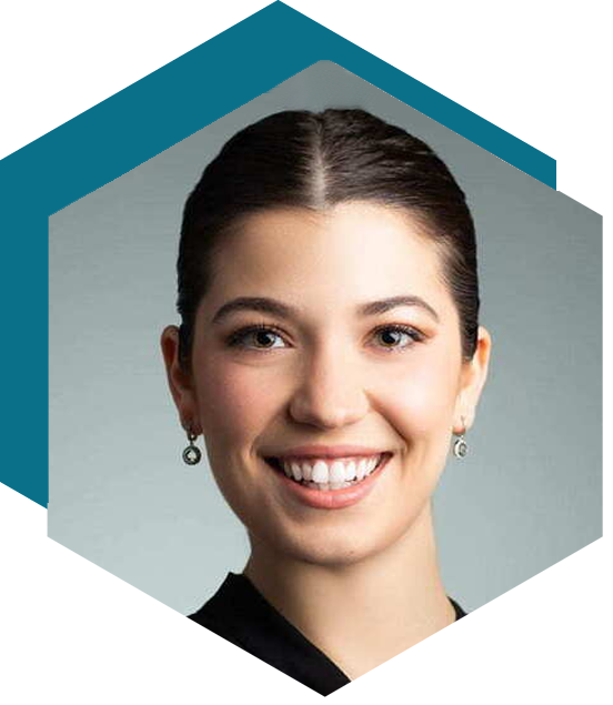 Smiling person with dark hair pulled back wearing small earrings and a black top, against a neutral gray background, framed in a hexagonal shape.