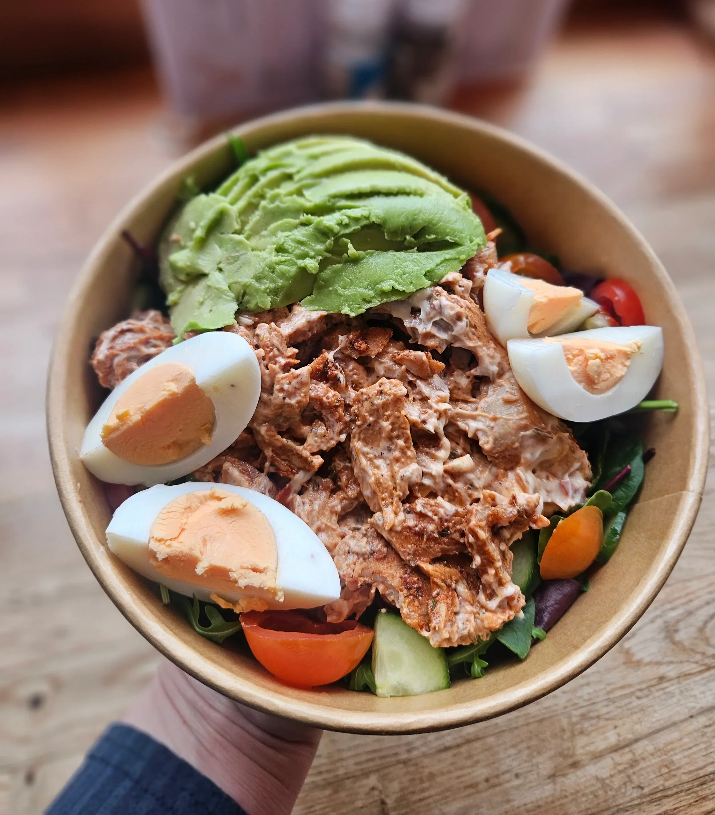 Bowl of salad with sliced avocado, hard-boiled eggs, cherry tomatoes, mixed greens, and shredded chicken.