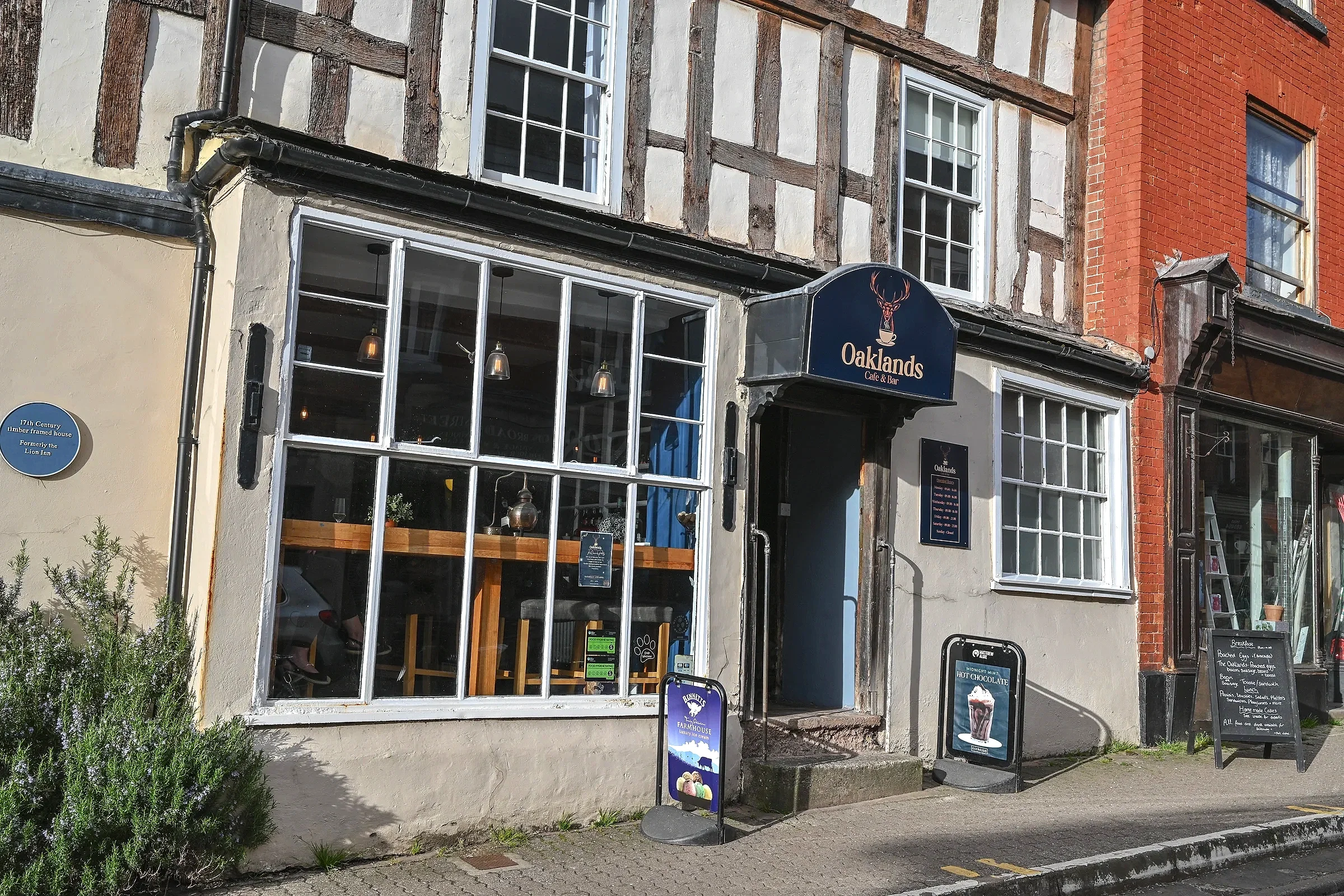 Front view of Oaklands Cafe & Bar with large windows, a sign with a deer logo, and two chalkboard menus outside on a sidewalk.