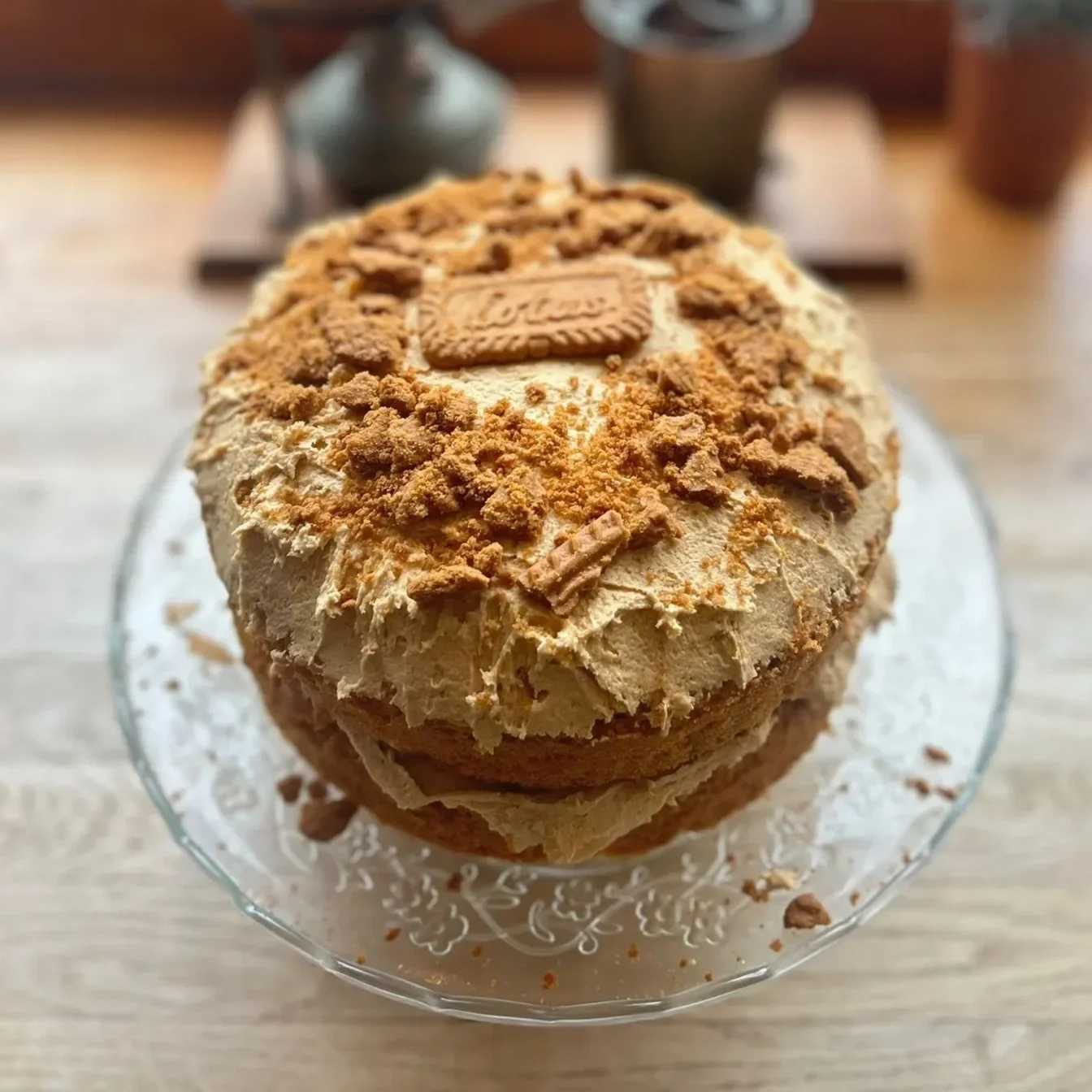 A layered cake topped with crumbled cookies and an Oreo cookie on top, served on a glass cake stand.