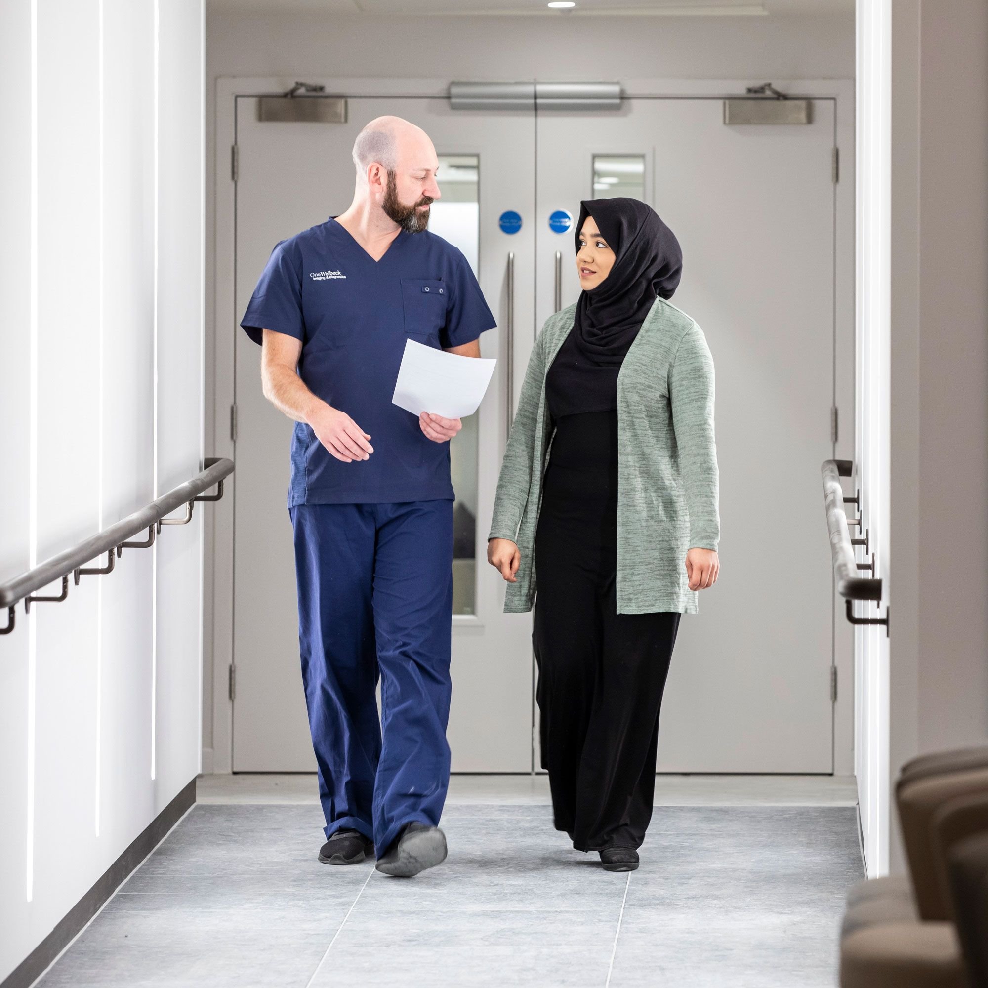 A male nurse and a woman walking in a hospital corridor.