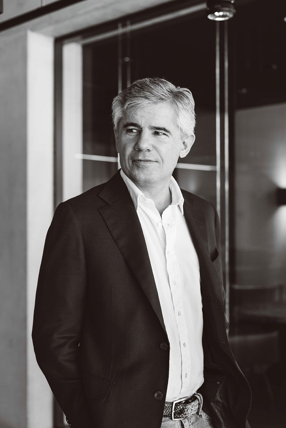 Black and white photo of a middle-aged man in a suit standing indoors, looking to the side with a slight smile.