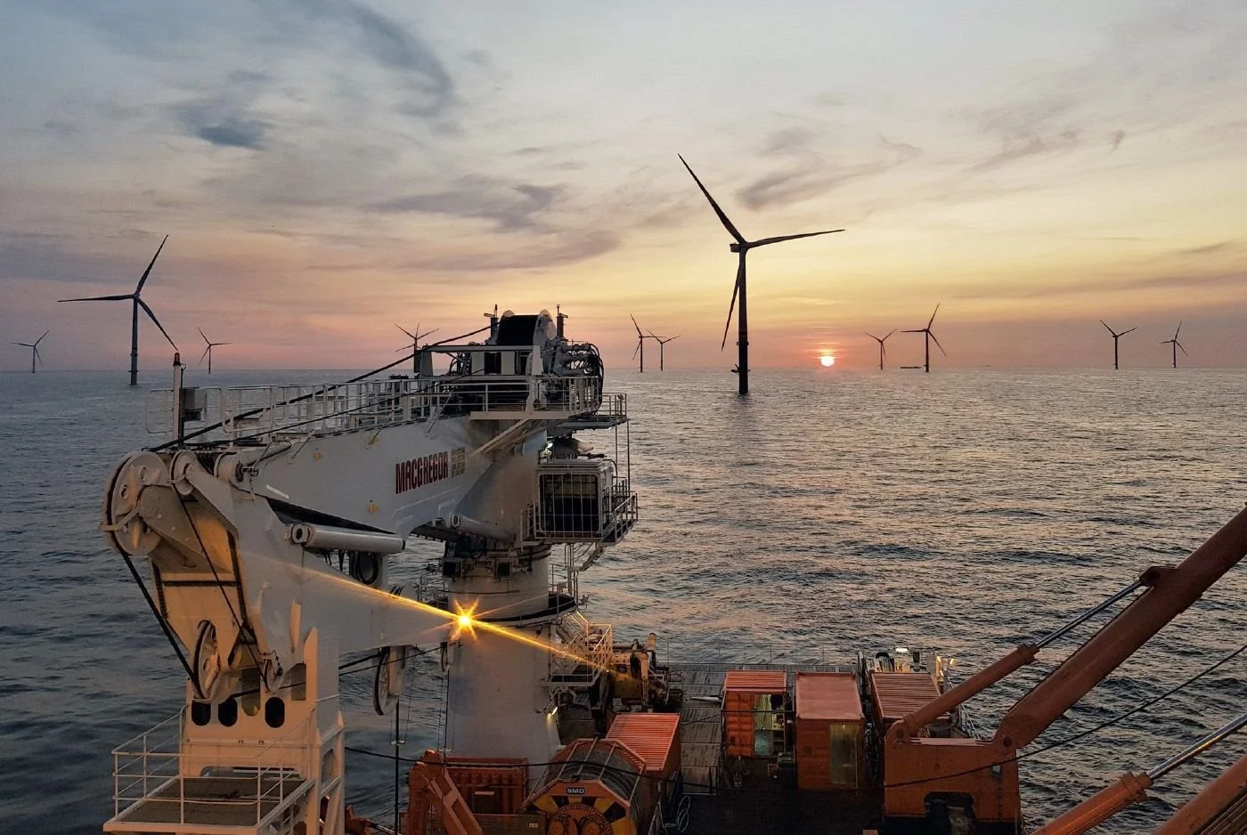 Offshore wind farm with several wind turbines at sea during sunset, viewed from a construction vessel.