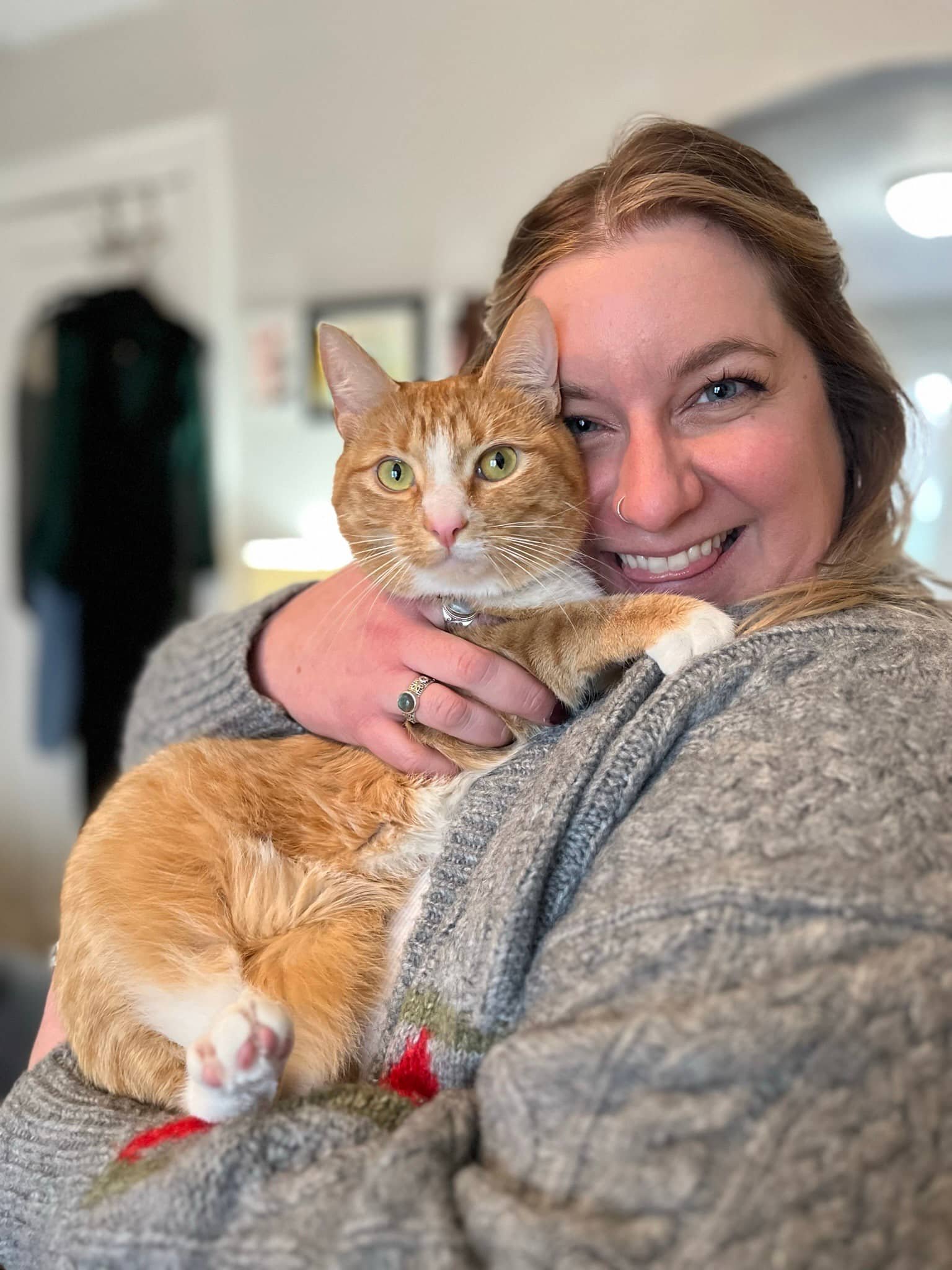 Close-up of a woman smiling and holding an orange tabby cat with green eyes.