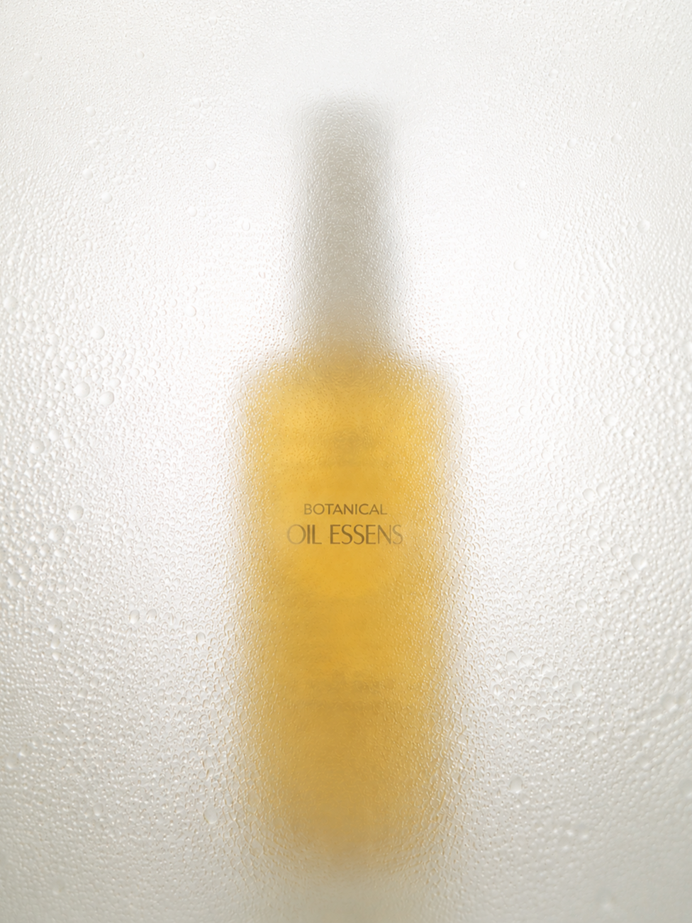 A bottle labeled 'Botanical Oil Essens' behind a foggy, condensation-covered glass surface.
