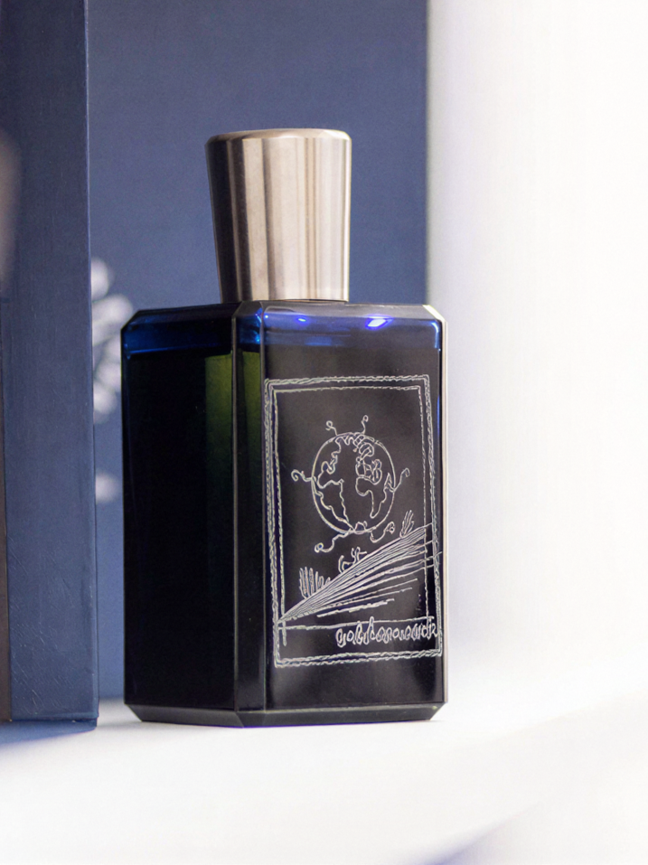 Blue perfume bottle with a silver cap, featuring a white line drawing of a globe and land on it.