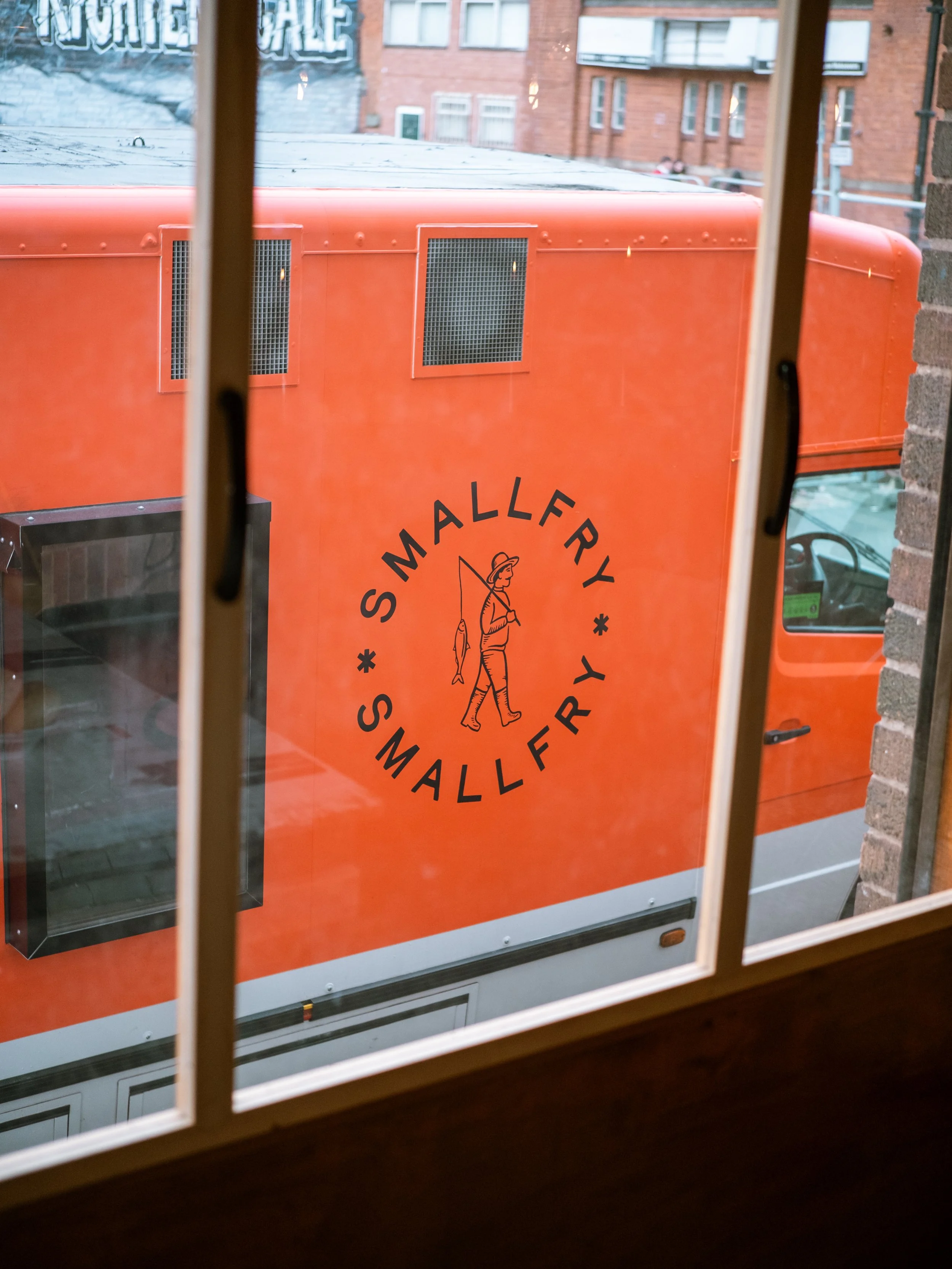 Orange food truck with the logo 'Smallfry' and an illustration of a person fishing, viewed through a window.