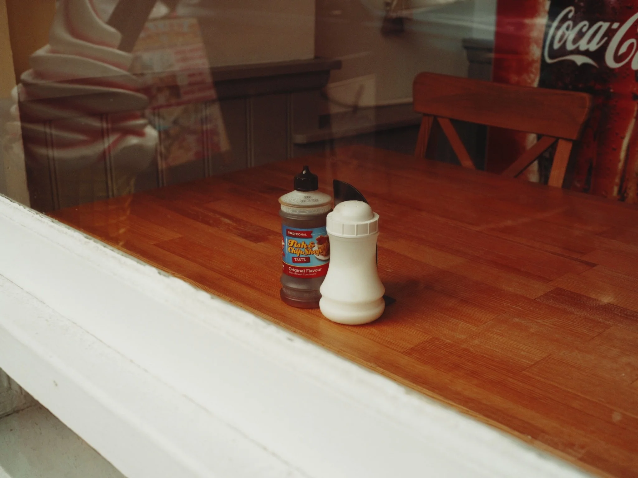 Condiments on a wooden table inside a restaurant, viewed through a glass window.