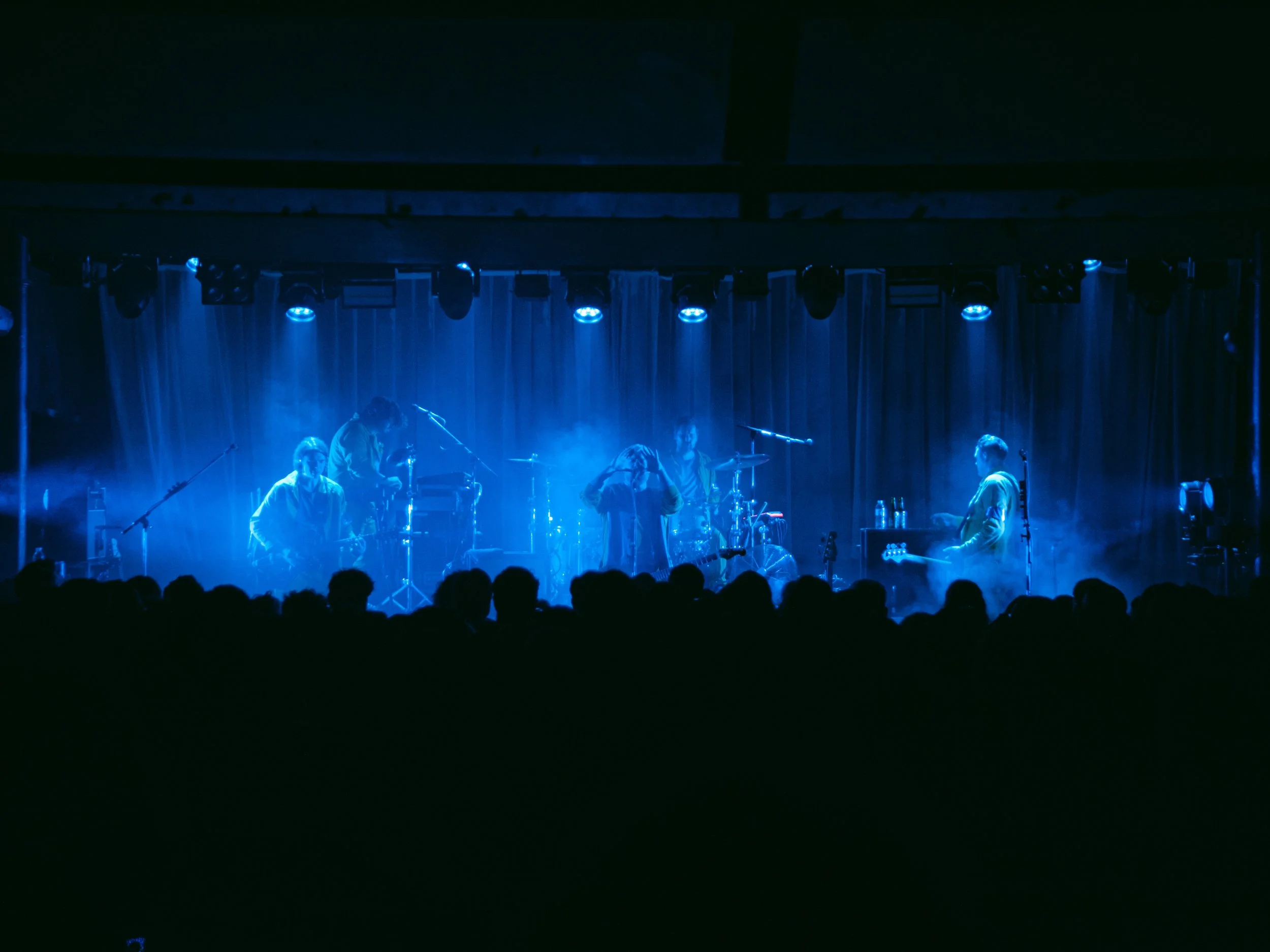 Band performing on stage with blue lighting, musical instruments, and audience silhouettes