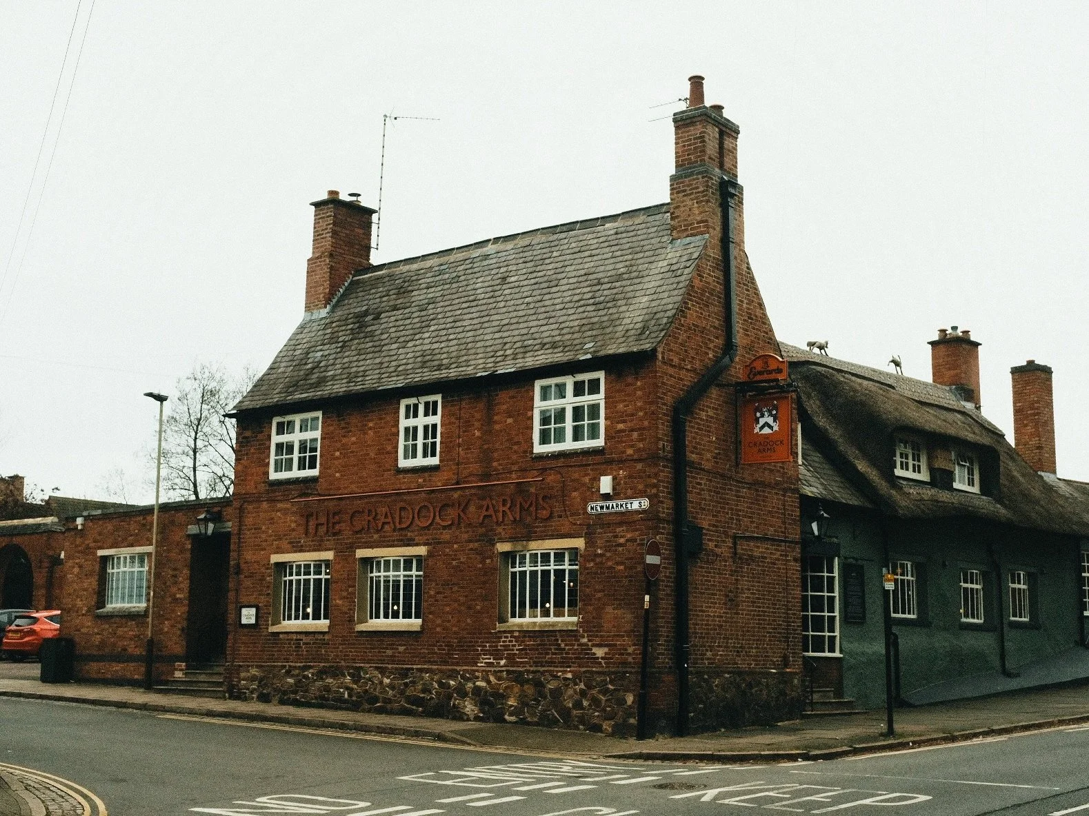 The exterior of The Gradock Arms pub, a brick building with multiple chimneys and white-framed windows, on a cloudy day.