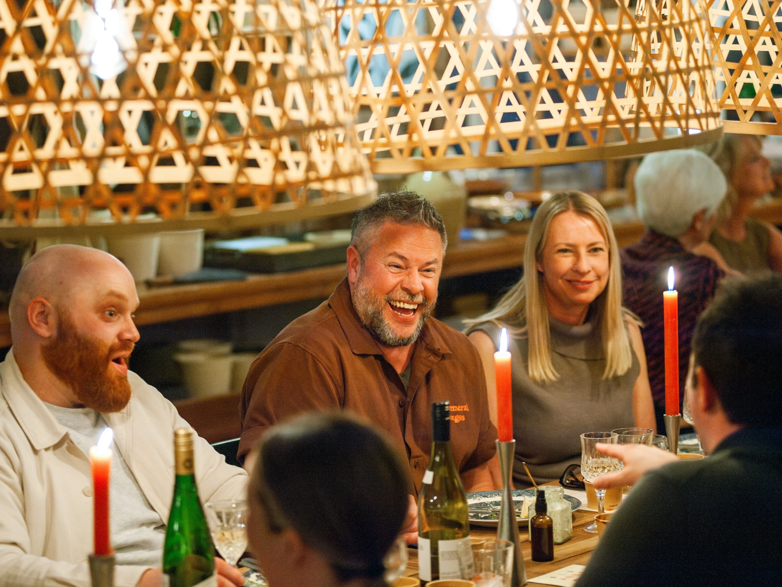 People enjoying a dinner at a restaurant, illuminated by candlelight, with smiling faces and lively conversation.