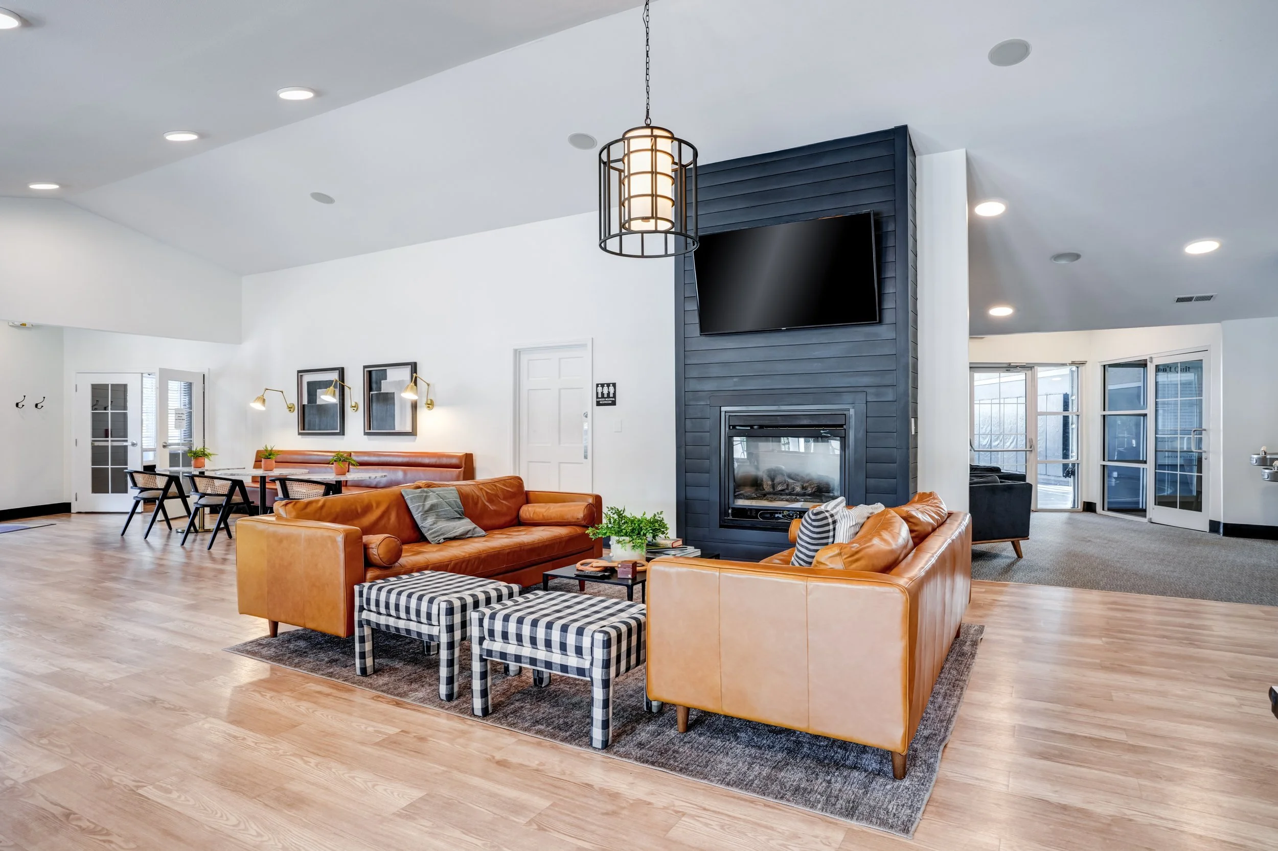 Clubhouse with tan leather sofas, a black and white checkered ottoman, and a wood-burning fireplace with a mounted TV above it. 