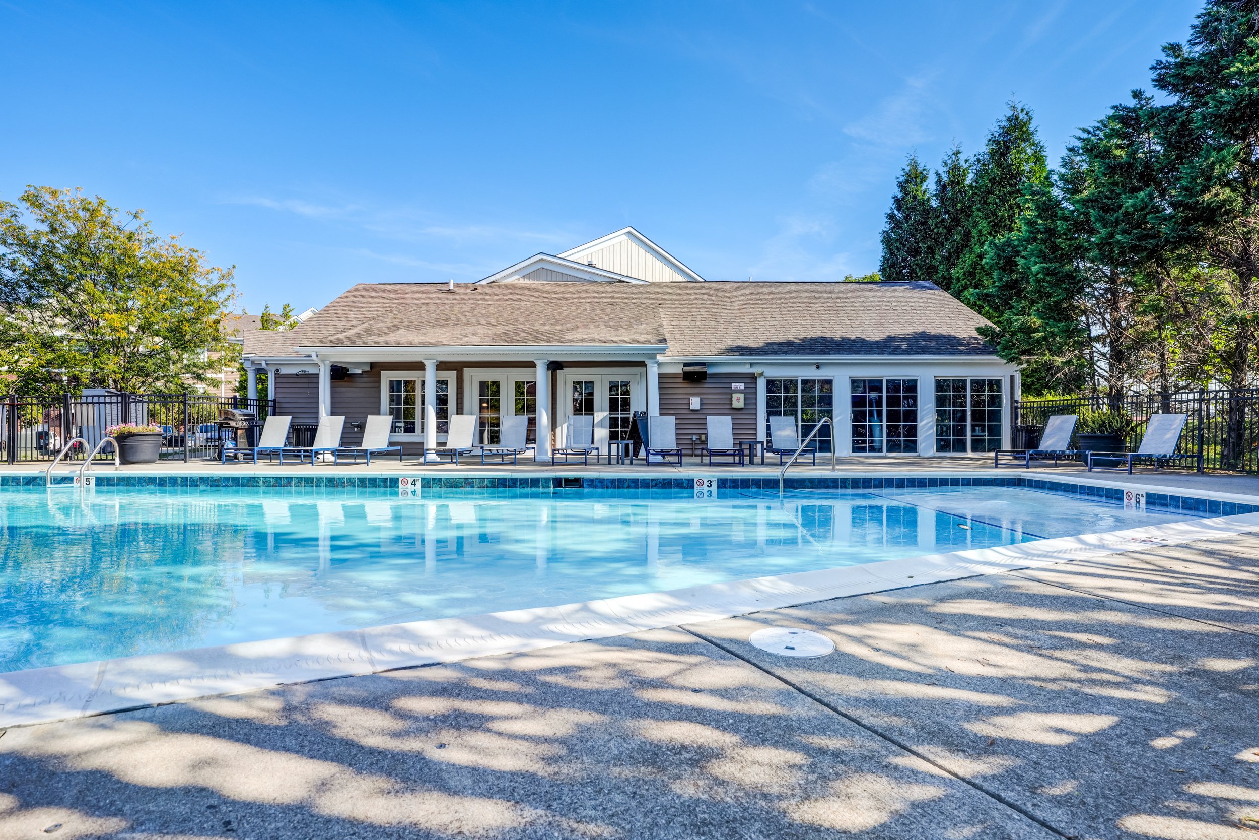 Outdoor swimming pool with lounge chairs and a building in the background under a clear blue sky.