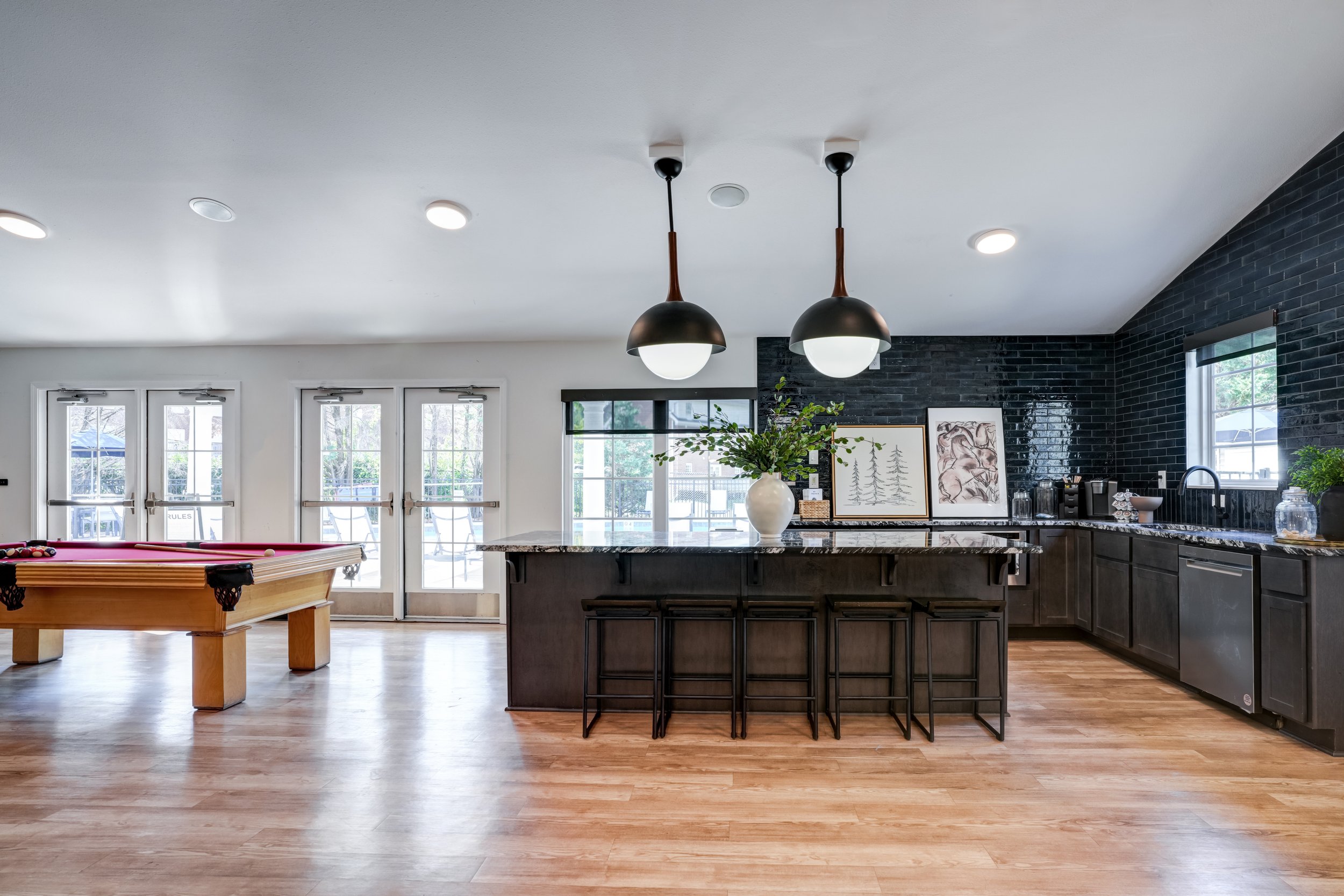 Modern kitchen with dark cabinets, white walls, black brick accent wall, marble island, two pendant lights hanging from the ceiling, and a ping pong table in the foreground.
