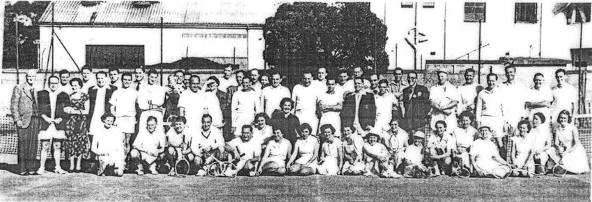 Group of men and women, likely a tennis team, posing on a tennis court with some holding rackets.