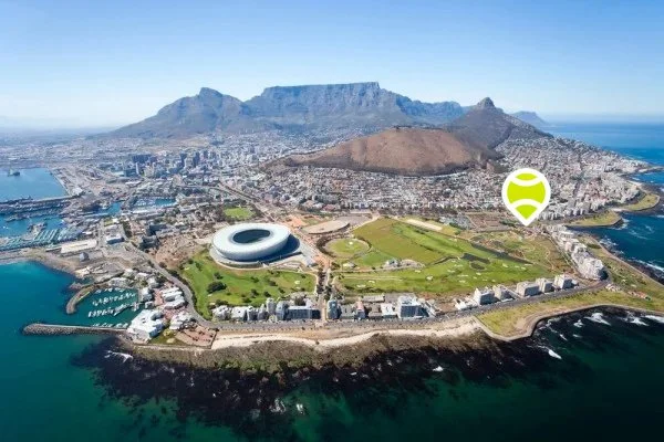 Aerial view of Cape Town, South Africa, featuring Table Mountain in the background, a stadium, golf course, and coastline.