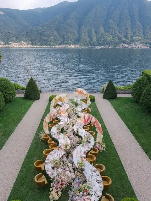 Long outdoor dining table decorated with flowers, set for a meal, overlooking a lake and mountains in the background.