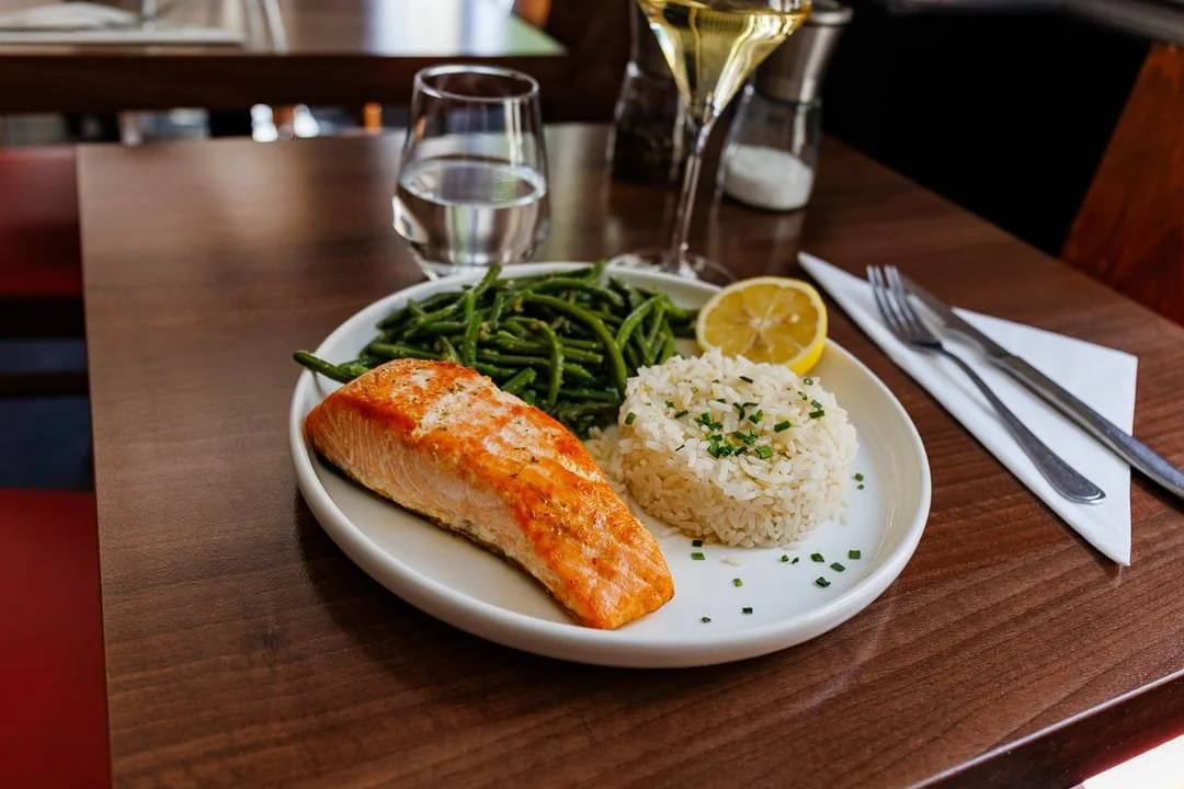 Assiette avec du saumon grillé, des haricots verts, du riz et un quartier de citron. Présenté avec des couverts et un verre d'eau, sur une table en bois.