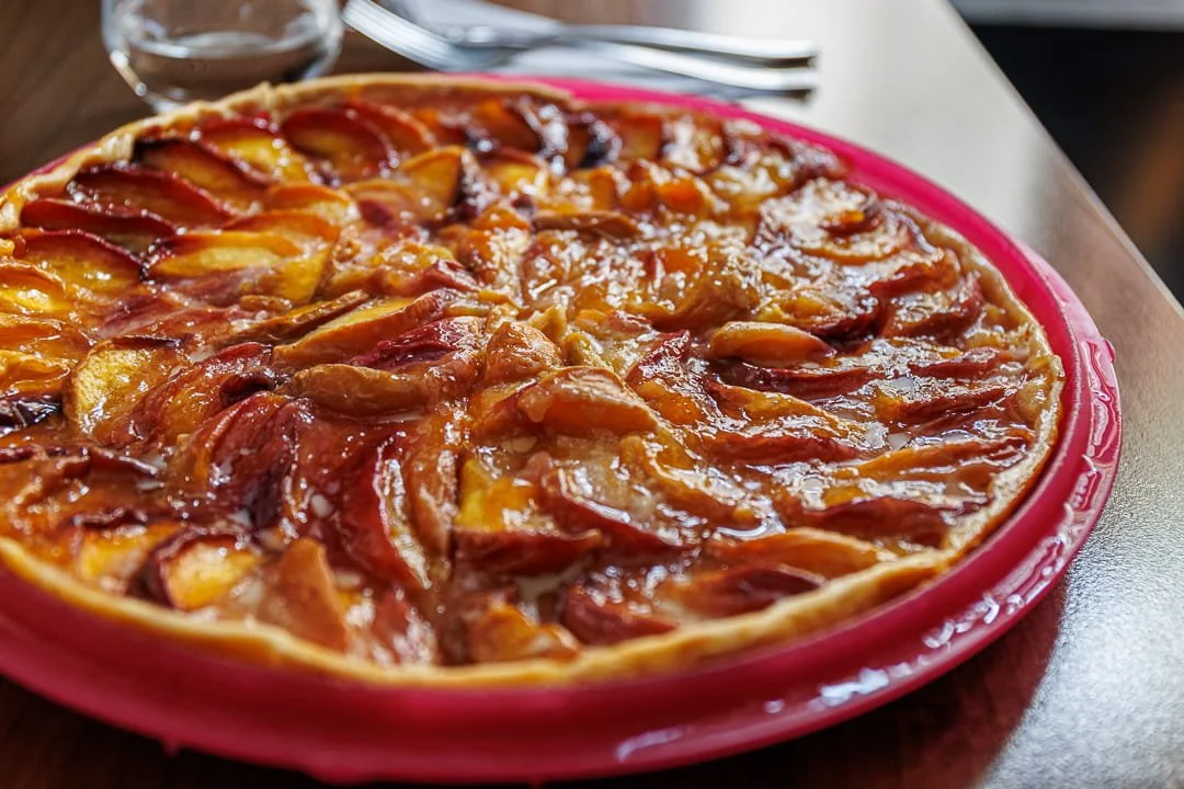 Une tarte aux pommes chaude dans un plat rouge, avec des cercles de pommes dorées et caramélisées.