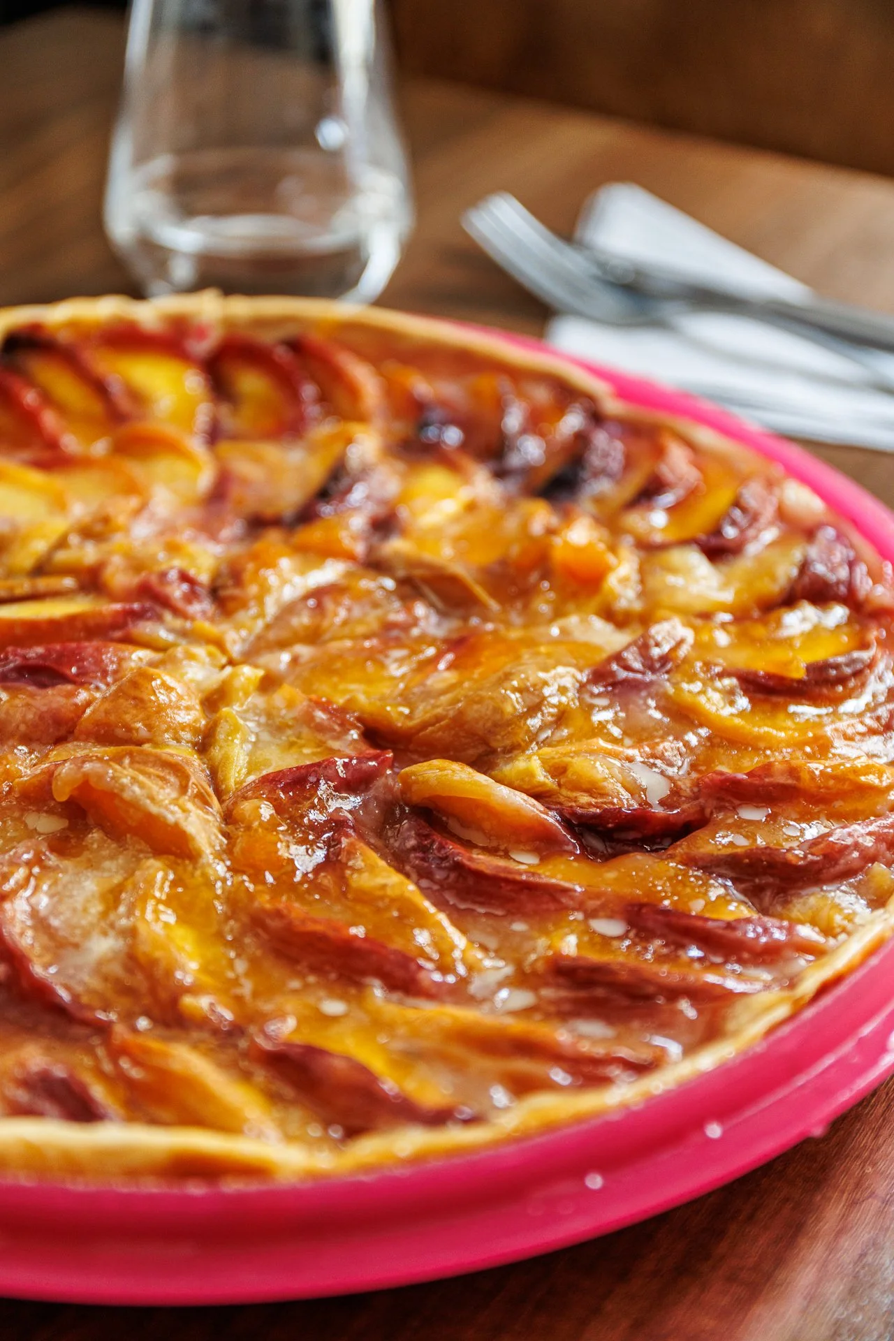 Une pizza aux ingrédients variés comme pepperoni, fromage, et légumes, dans un plat rose, placée sur une table en bois.