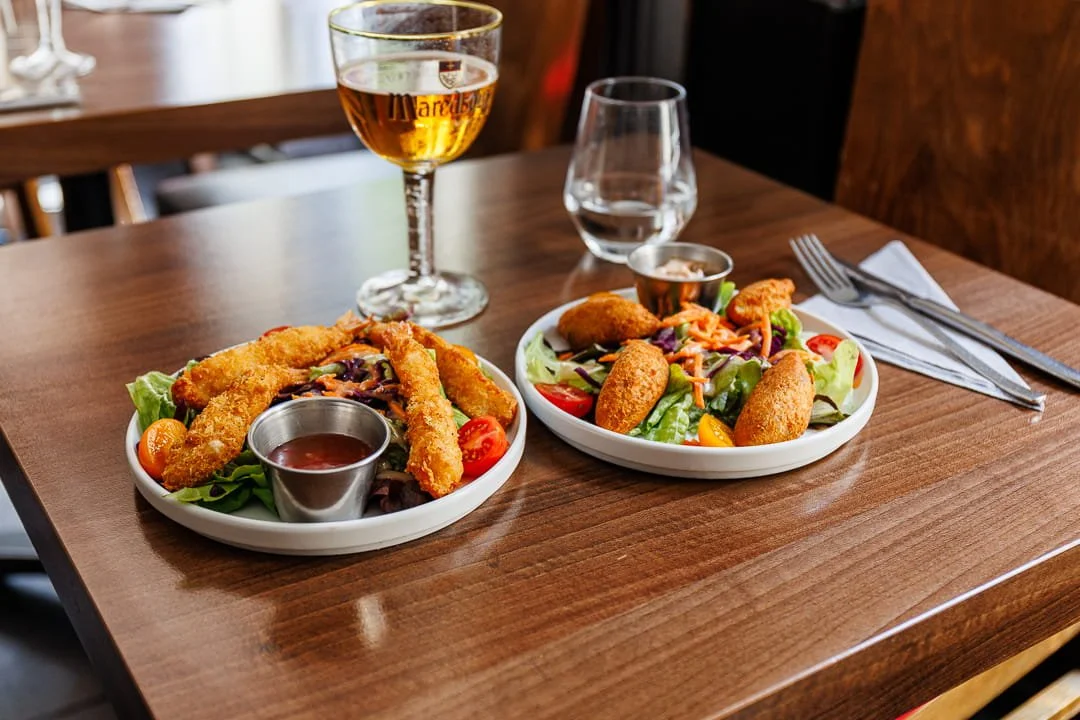 Plateau de salade avec des morceaux de poulet pané, accompagnée de légumes et de sauce, avec un verre de vin blanc, un verre d'eau et des couverts sur une nappe blanche.