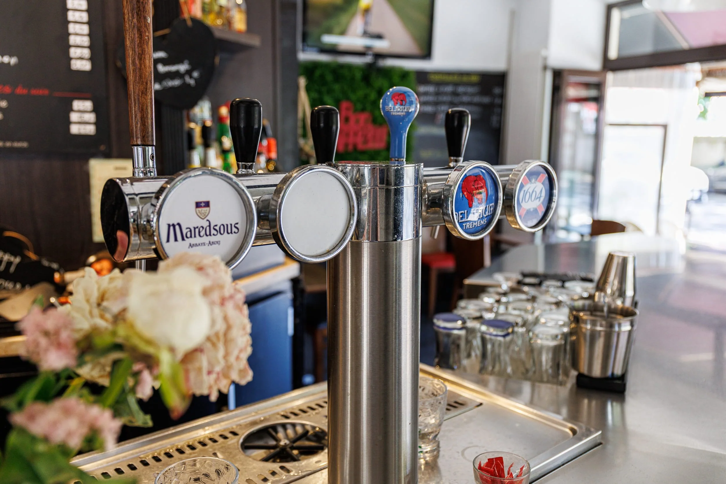 Un distributeur de bière avec quatre poignées, axé sur une bière avec un logo de bulles. En arrière-plan, un bar ou un restaurant avec des écrans et des décorations.
