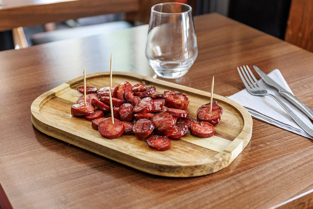 Plate de saucisses de Provence sur une planche en bois, avec un verre d'eau à côté, à une table en bois.