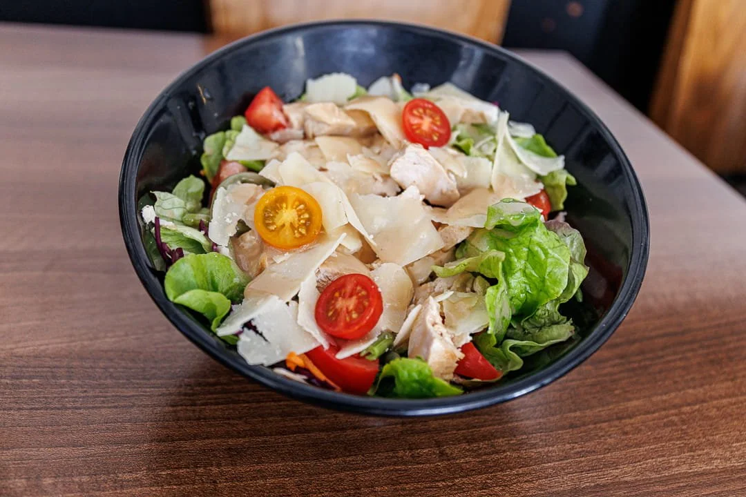 Salade composée dans un bol noir avec laitue, tomates cerises jaunes et rouges, copeaux de parmesan, morceaux de poulet et autres légumes